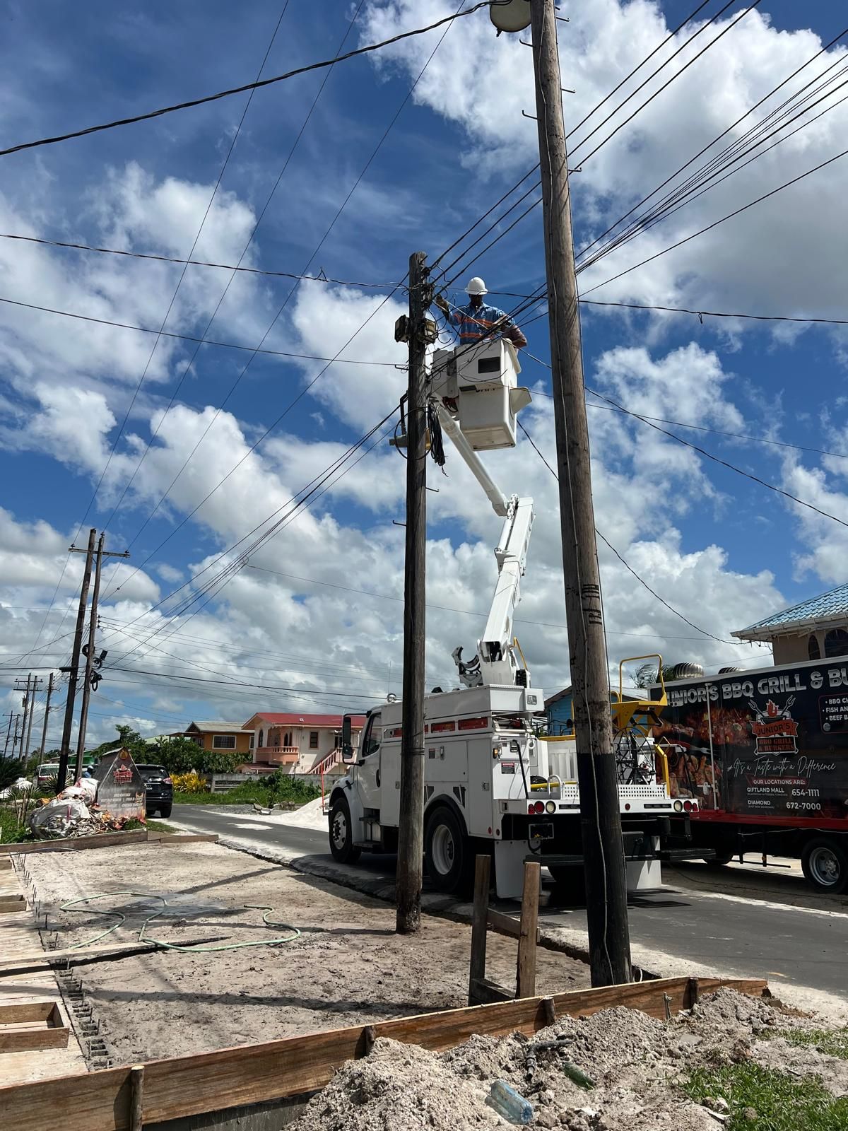 Bucket truck lifting a lineman to a power pole under blue sky